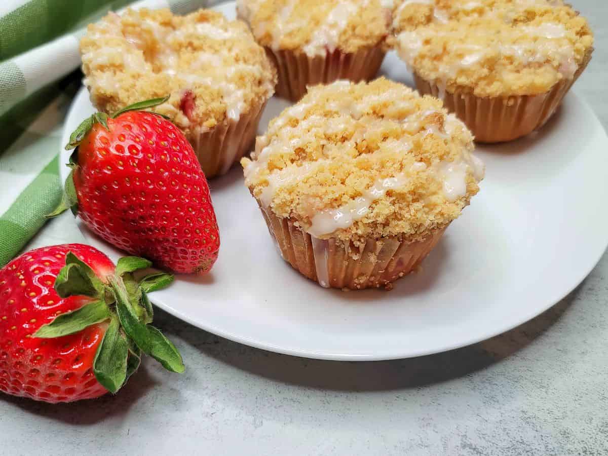 Strawberry streusel muffins on a white plate with strawberries.