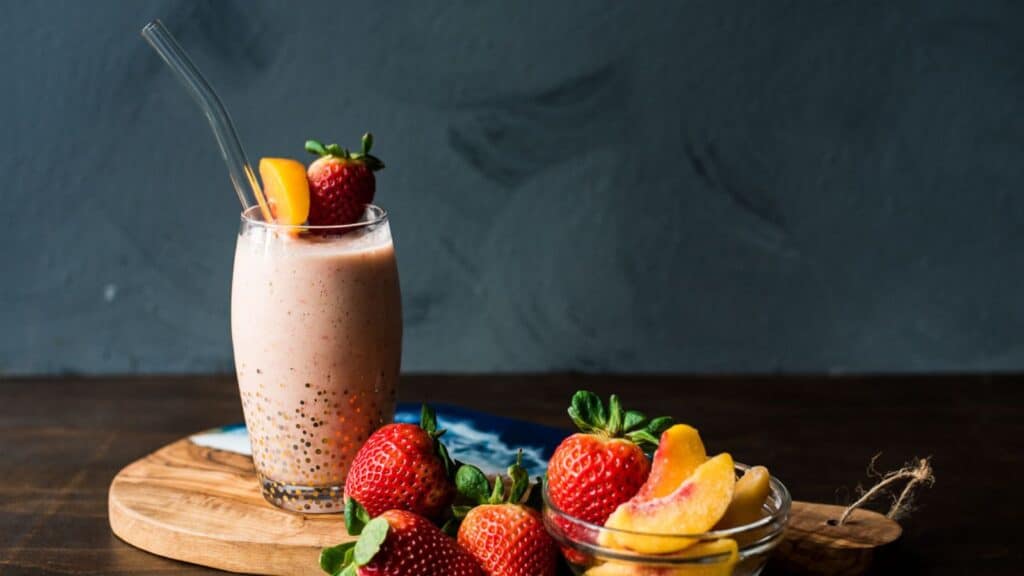 A smoothie with strawberries and peaches on a wooden board.