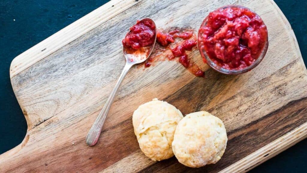 Strawberry jam and scones on a wooden cutting board.