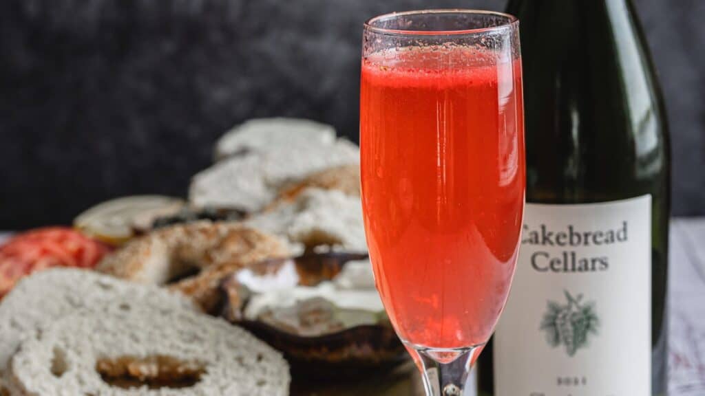 A glass of wine and a baguette on a table next to a bottle of wine.