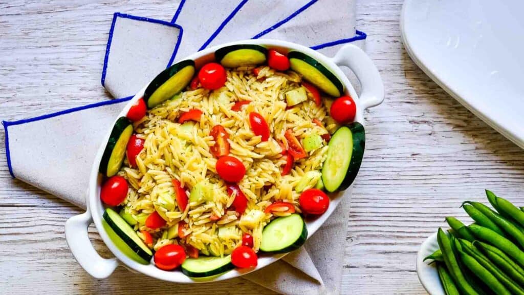 A white dish with noodles, tomatoes and cucumbers.