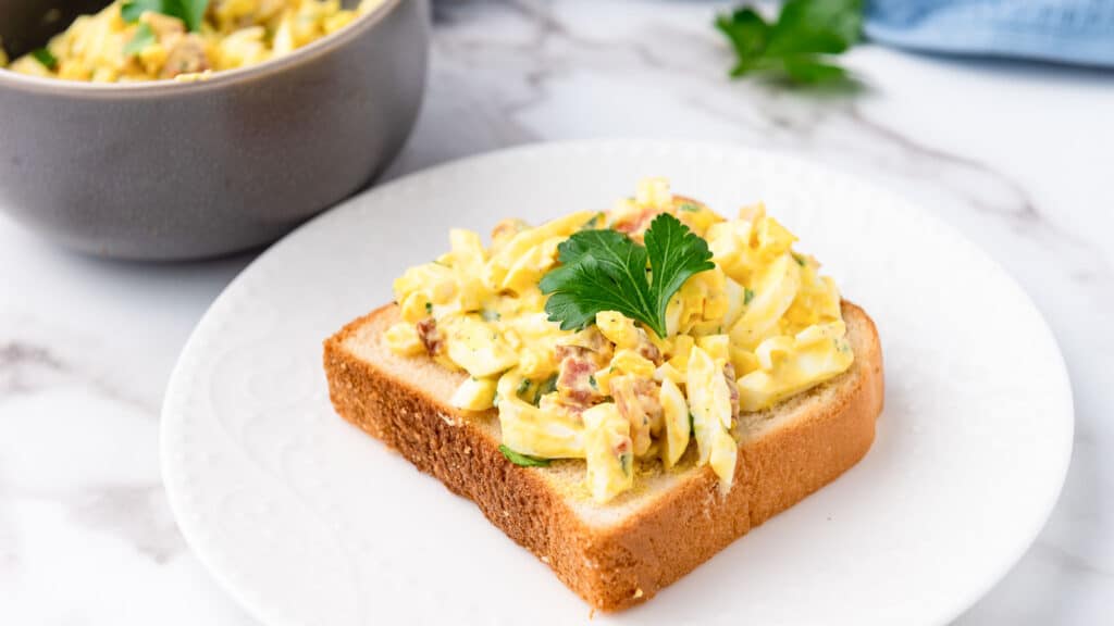 An egg salad sandwich on a slice of bread with parsley.