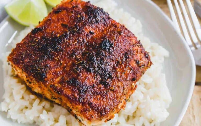 A piece of salmon on a plate with rice and lime wedges.