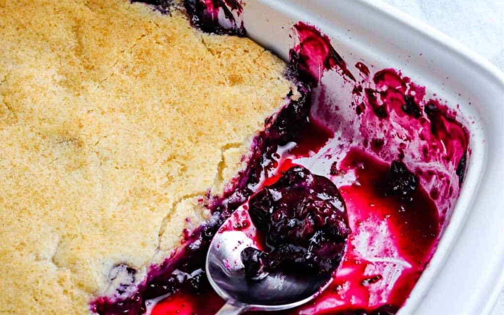 Blueberry cobbler in a white dish with a spoon.