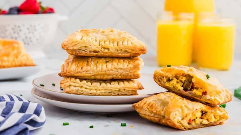 A stack of breakfast pastries on a plate next to a glass of orange juice.