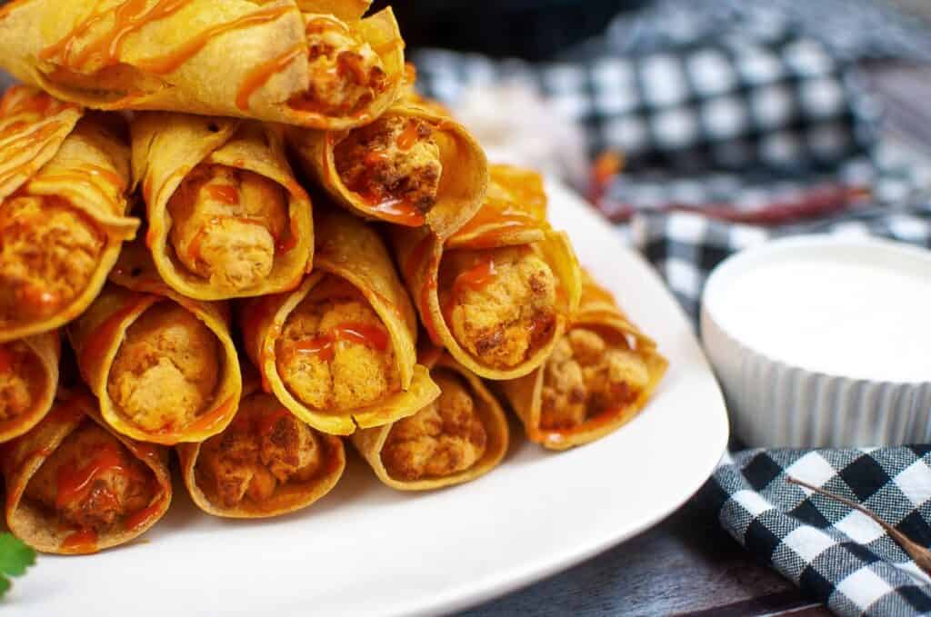 Chicken taquitos with sour cream on a plate.