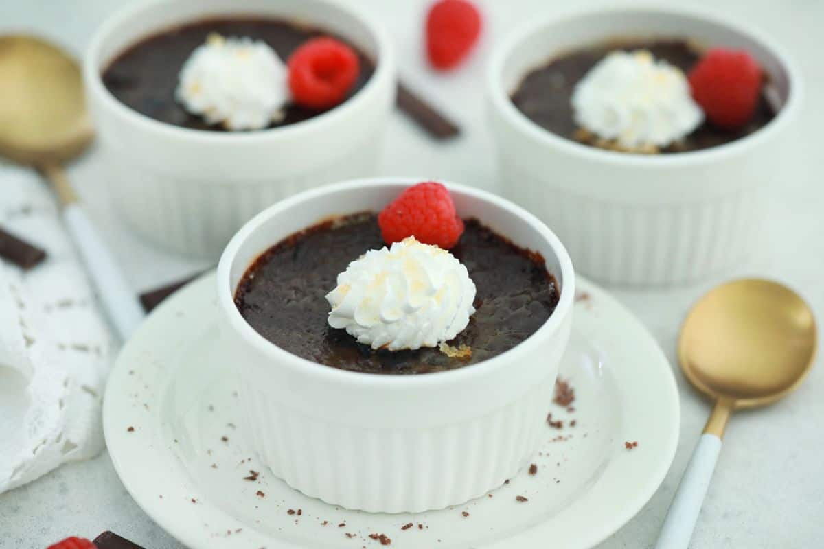 Three cups of chocolate pudding with whipped cream and raspberries.