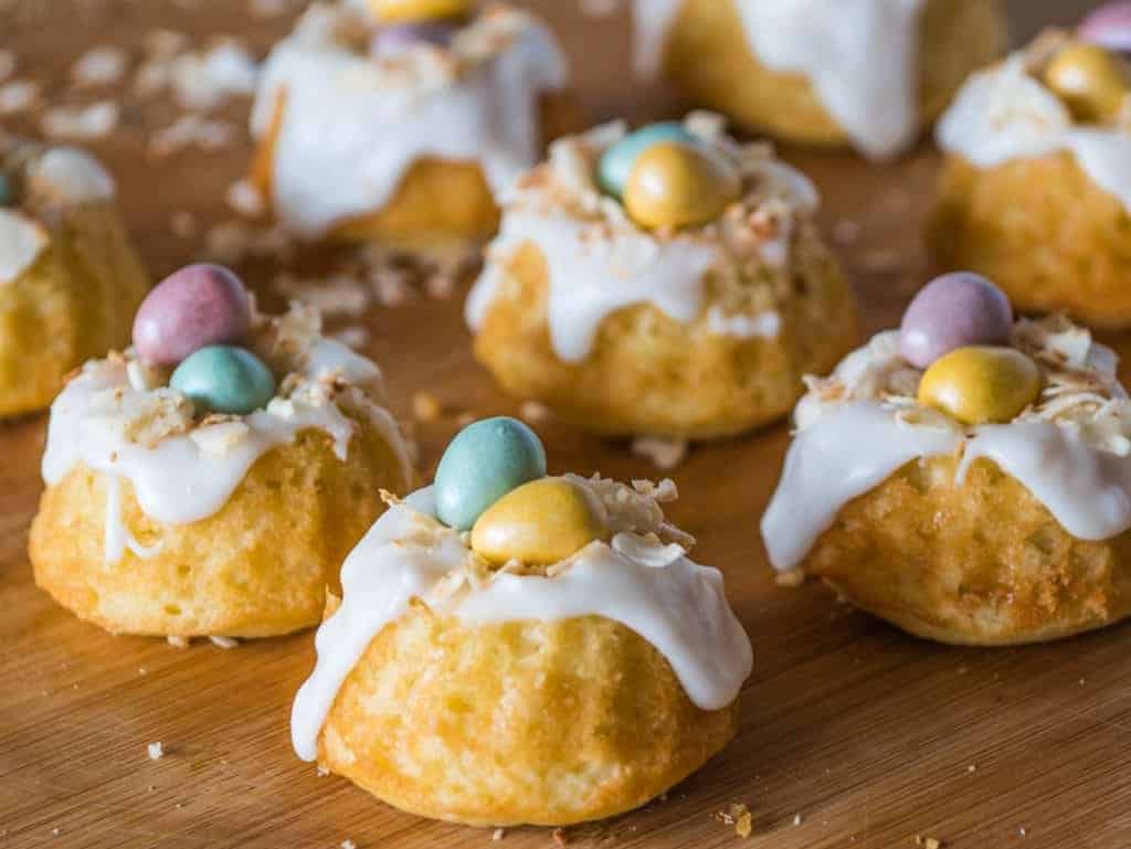 Easter buns with icing and eggs on a wooden cutting board.