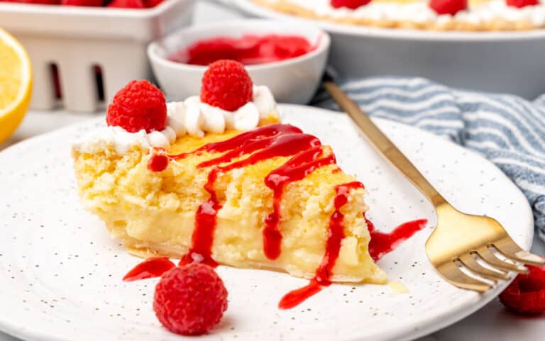 A slice of lemon sponge pie with raspberries and whipped cream.