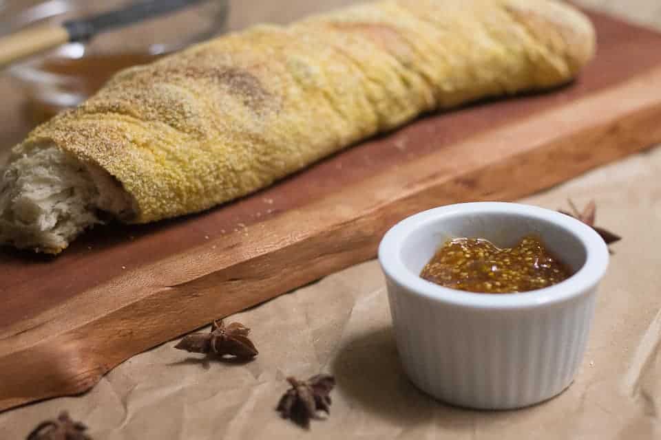 A bread roll on a cutting board next to a small bowl of sauce.