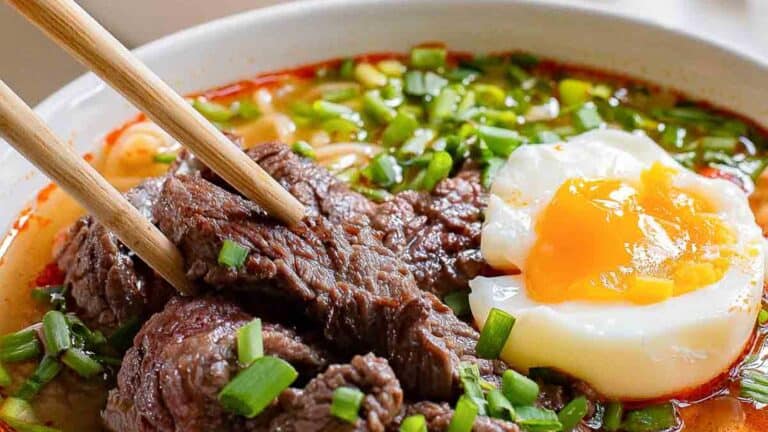 A bowl of beef noodle soup with an egg and chopsticks.