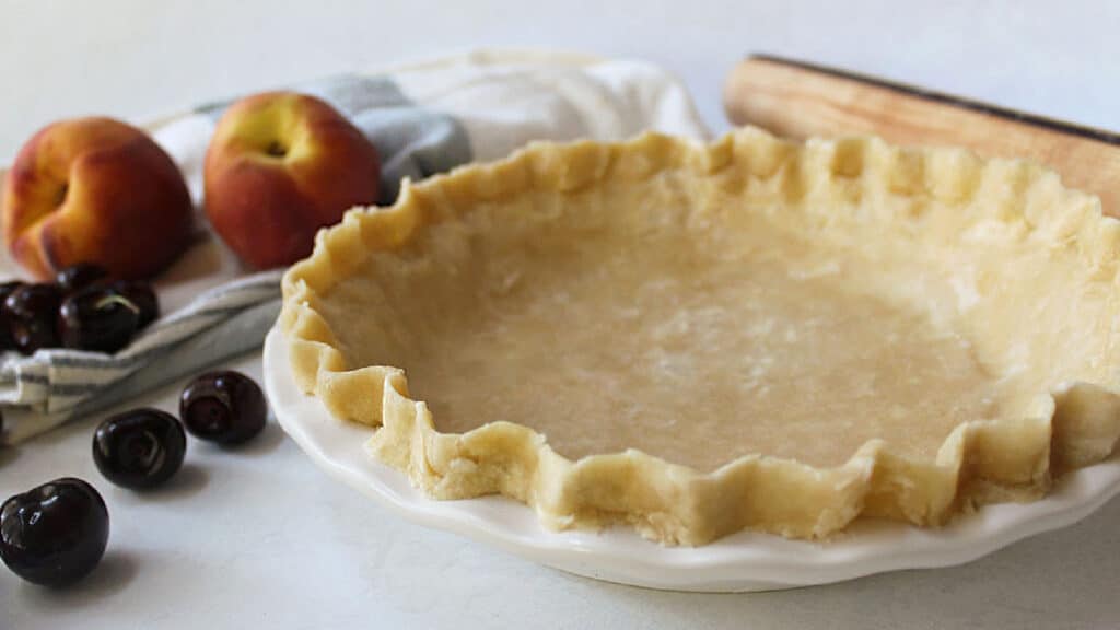 An unbaked pie crust with cherries and peaches in the background.