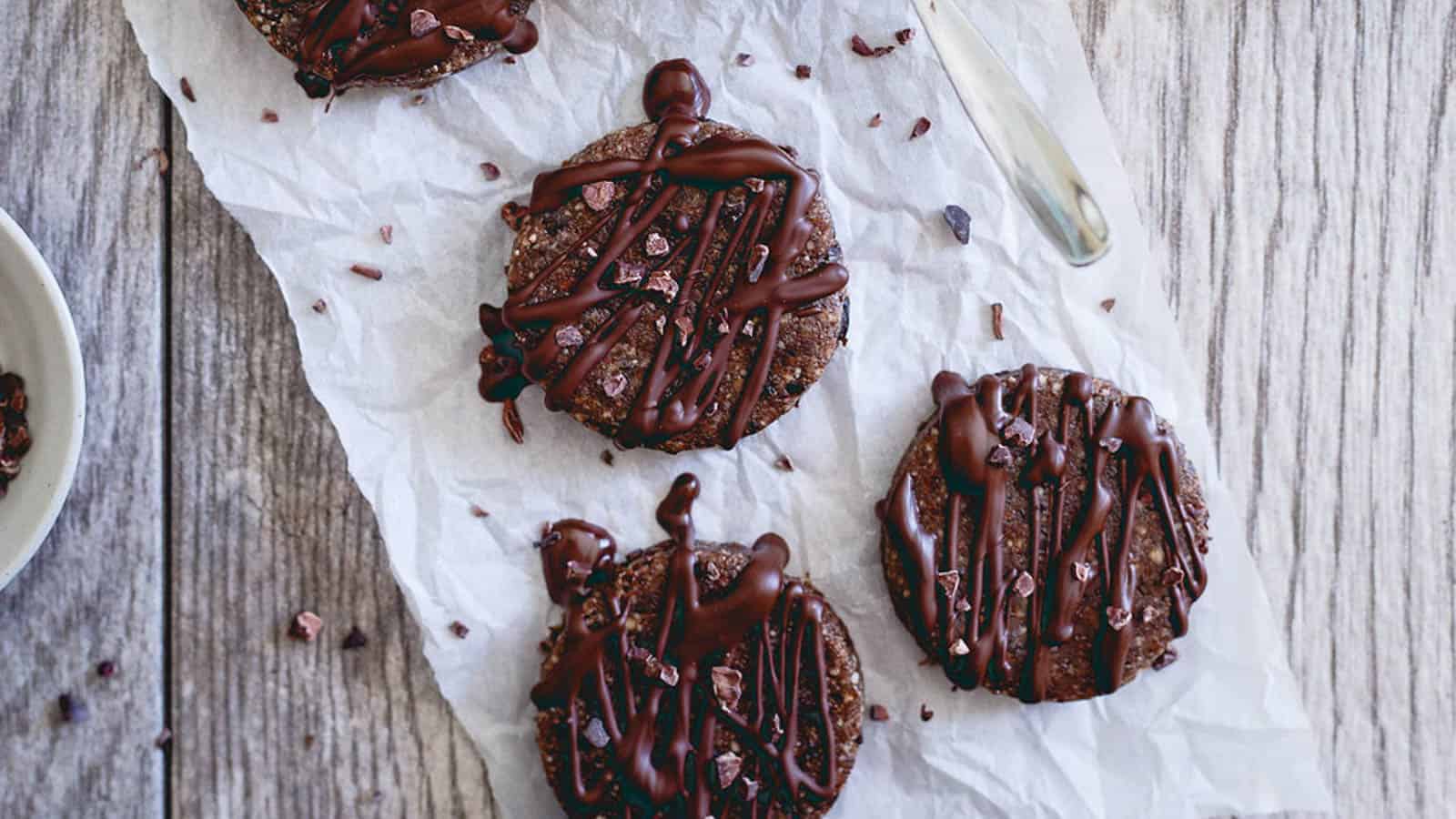 Raw brownie bites on parchment paper drizzled with chocolate.