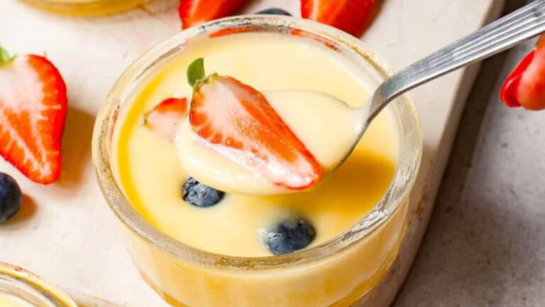 A spoon is being poured into a jar of lemon custard with strawberries and blueberries.