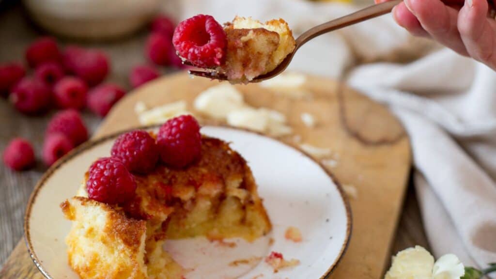 A person eating a piece of raspberry bread pudding on a plate.