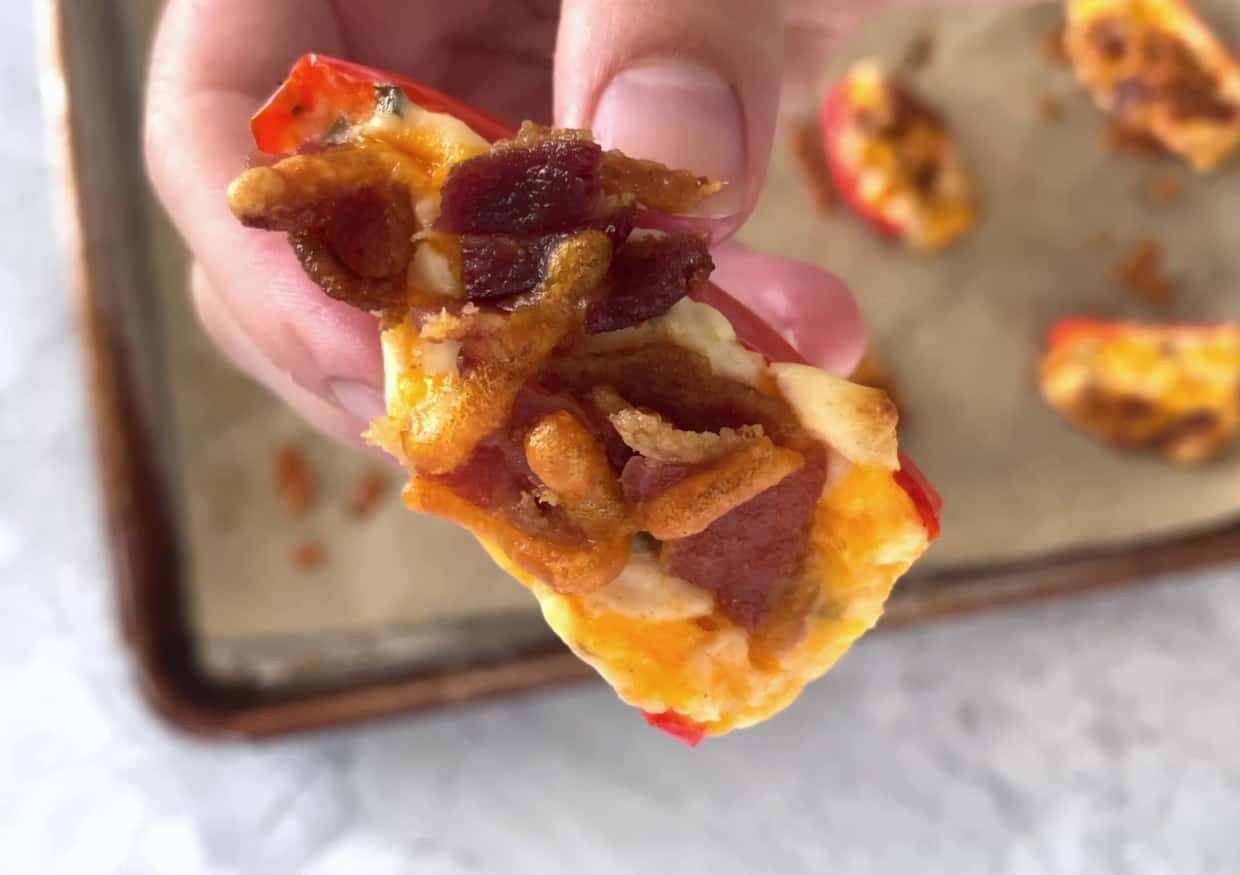 A hand holding a mini pepper topped with bacon.