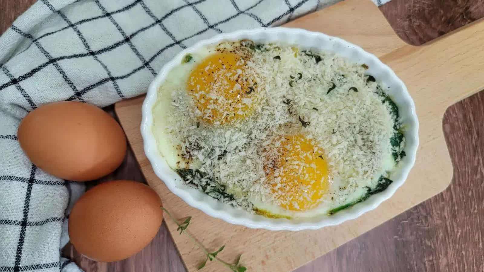 Baked eggs with spinach and parmesan on a wooden cutting board.