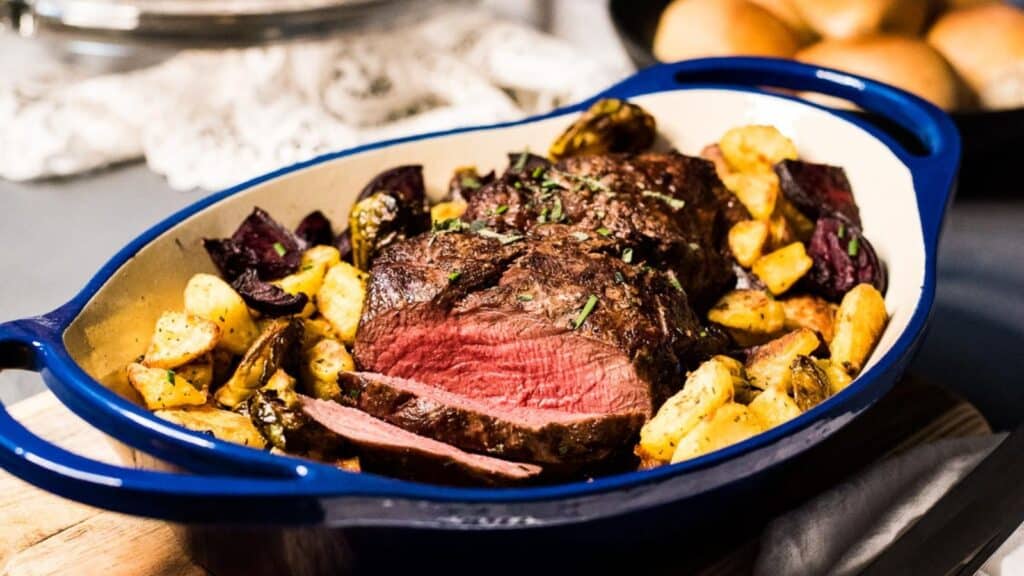 Roast beef with herbs and roasted potatoes in a blue enameled cast-iron dish.