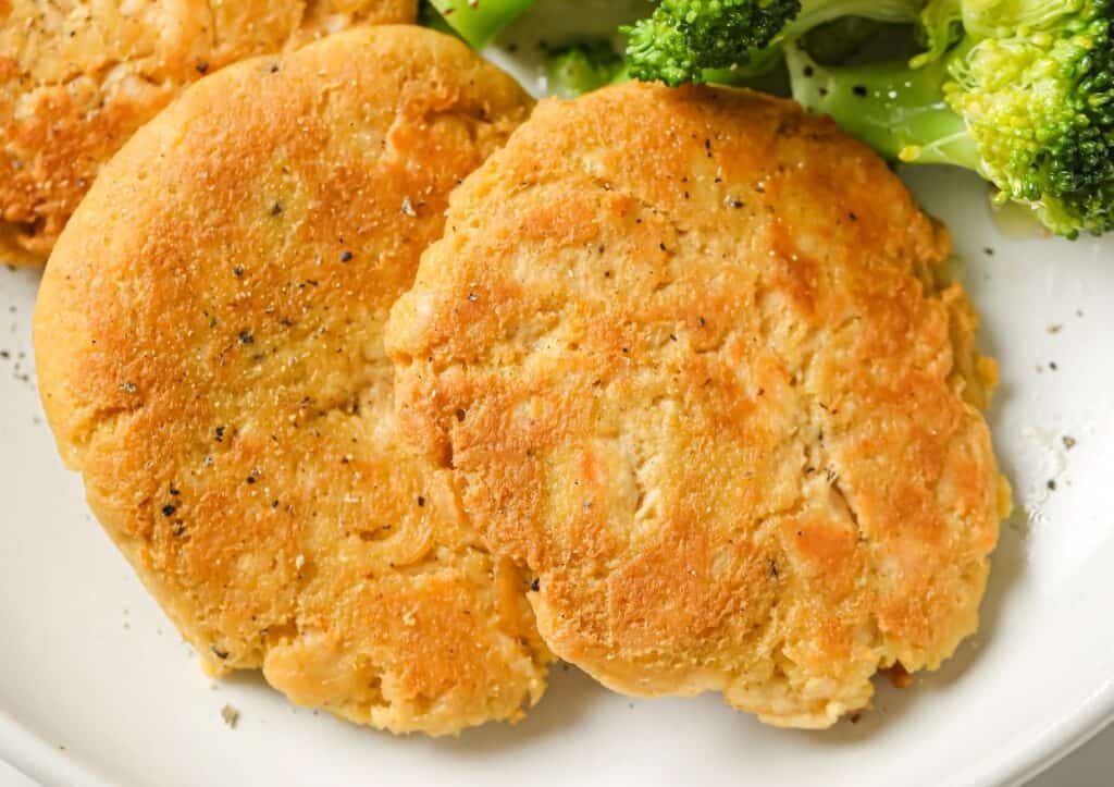 Golden-brown chicken patties on a plate with broccoli on the side.