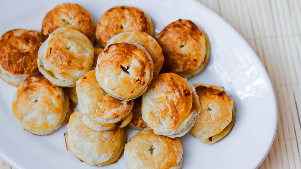 A plate of golden-brown, flaky pastry bites displayed on a white plate.