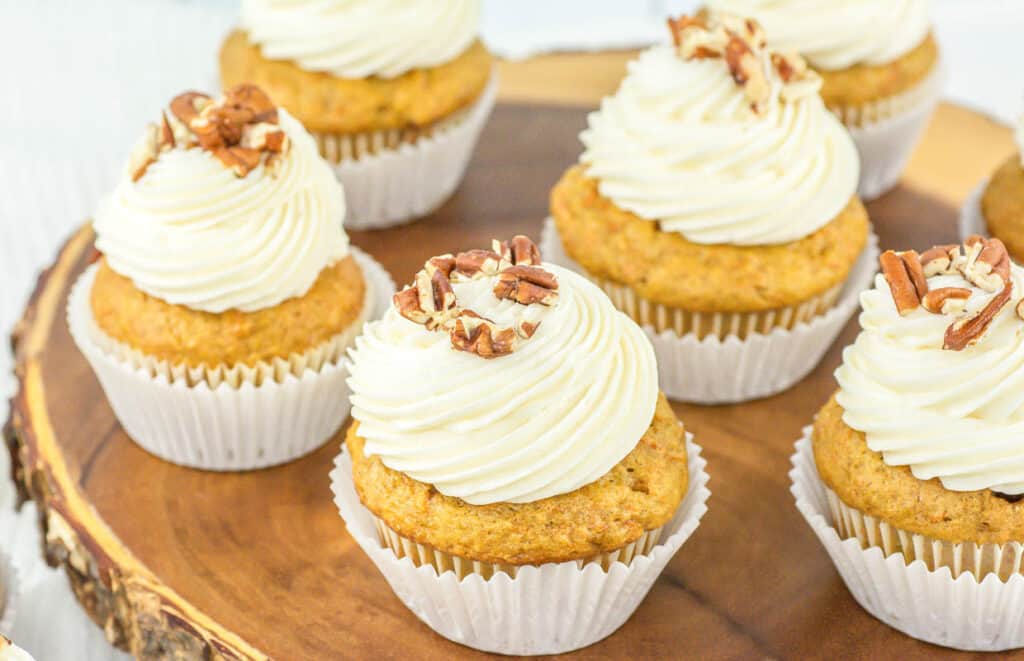 Frosted cupcakes with pecan toppings presented on a wooden platter.