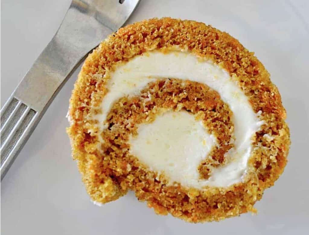 A slice of pumpkin roll dessert with cream filling on a white plate with a fork.