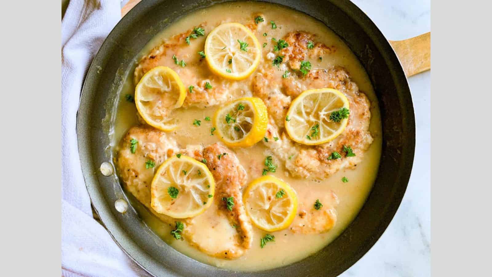 A skillet filled with lemon chicken in sauce with lemon slices.