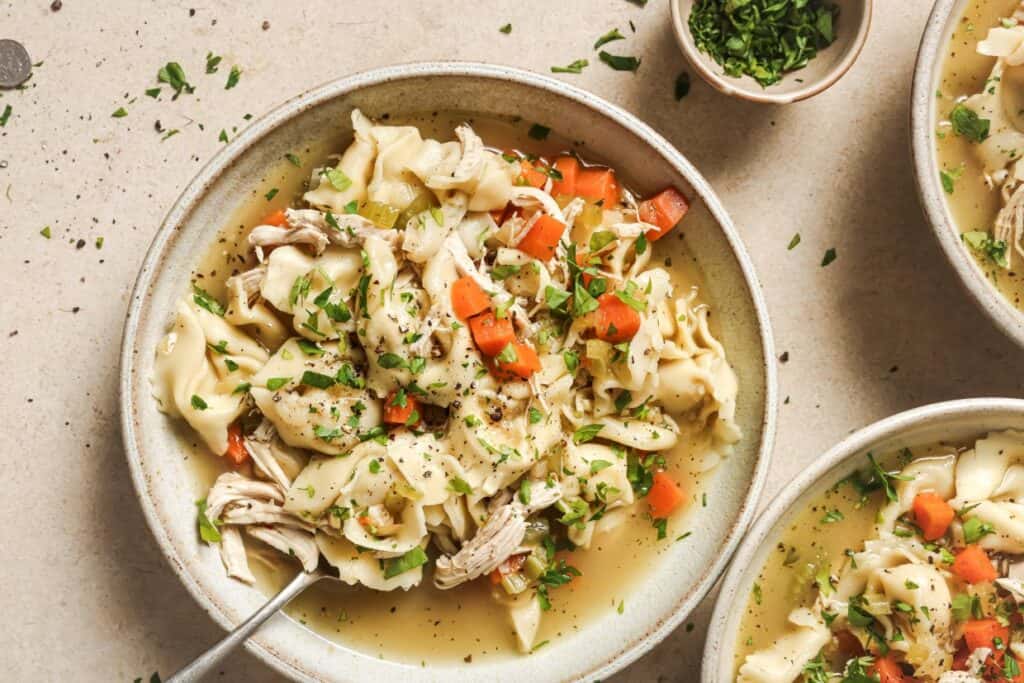 A bowl of chicken tortellini soup with chopped vegetables and herbs.