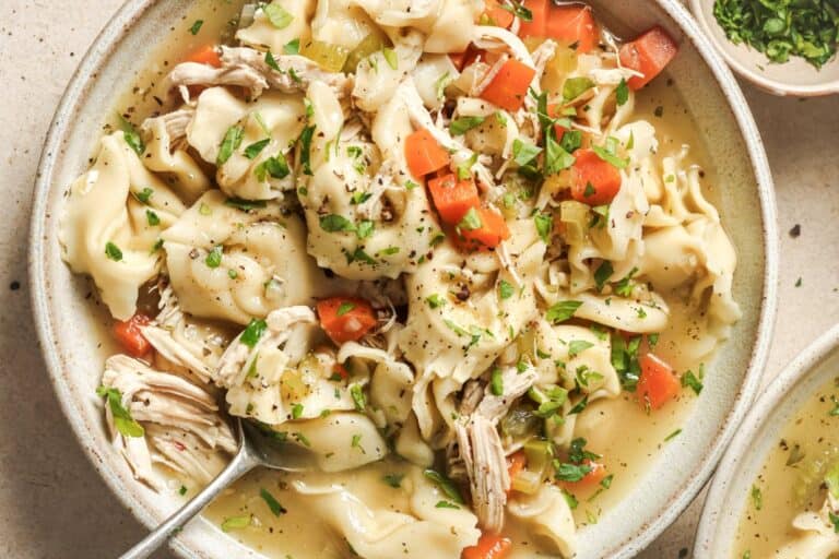 A bowl of chicken tortellini soup garnished with herbs.