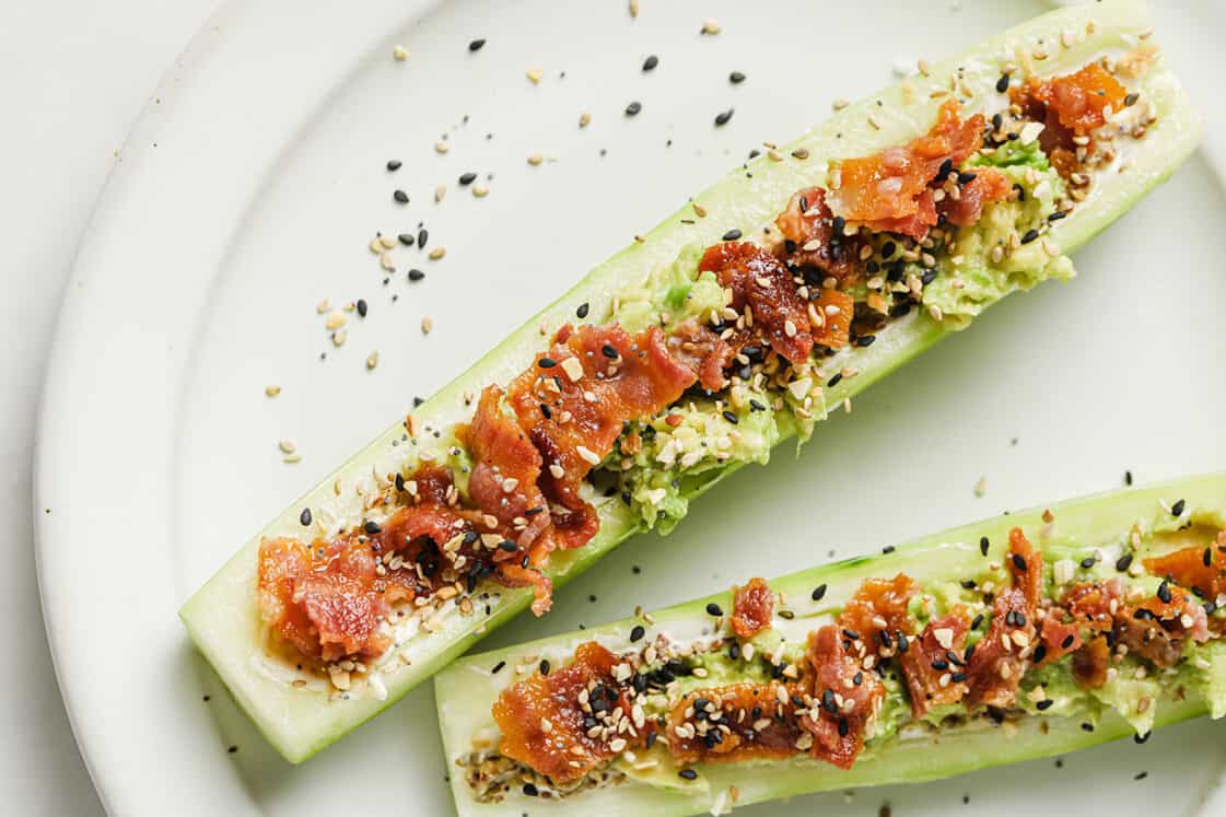 Cucumber boats topped with avocado, bacon, and sprinkled with seasoning.