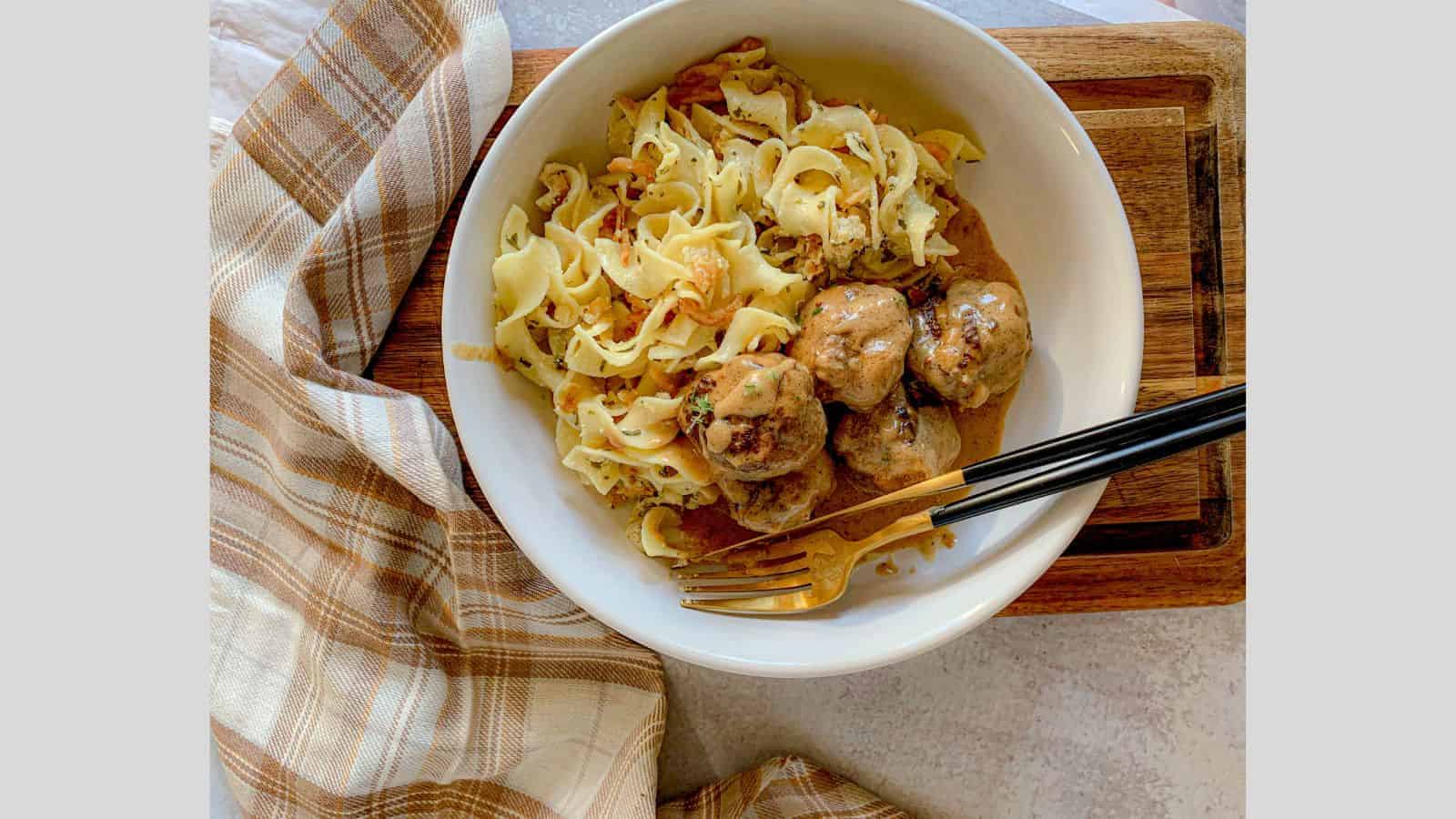 A bowl filled with French onion noodle casserole and a side of meatballs.