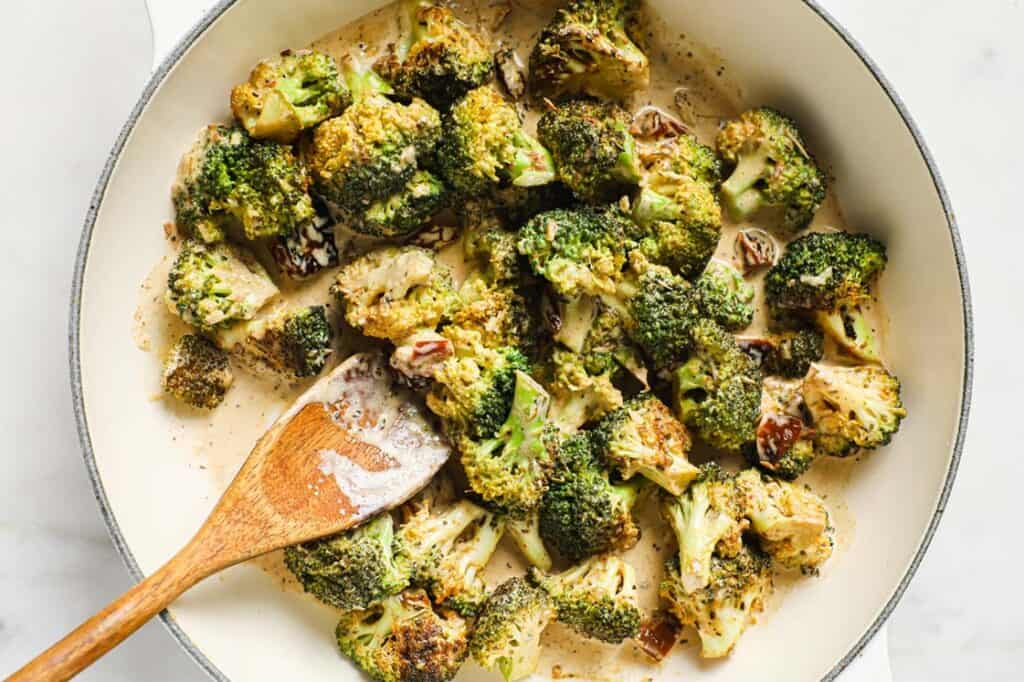 Sautéed broccoli in a pan with seasonings and a wooden spoon.