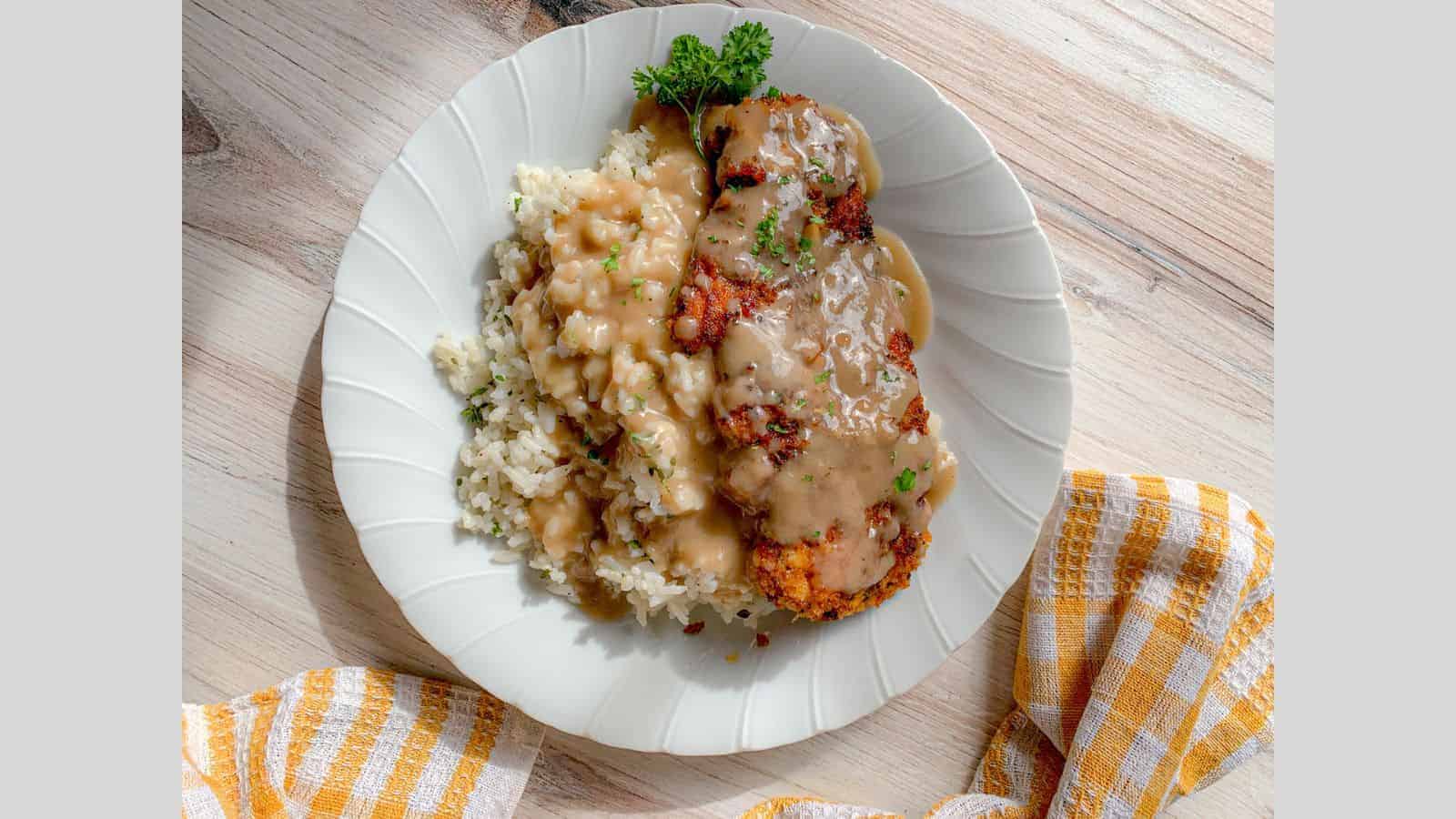 A dinner plate filled with pan fried chicken, rice, and gravy.