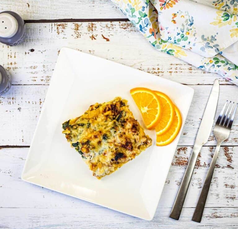 A white plate with a slice of Croissant breakfast casserole and orange next to it.