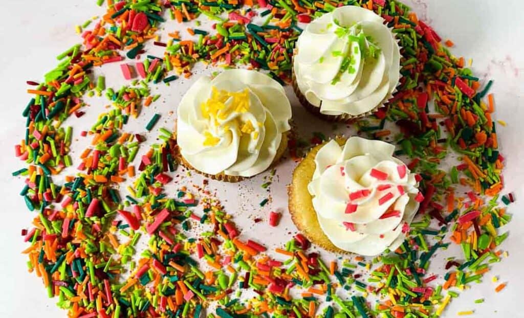 Three cupcakes surrounded by colorful sprinkles.