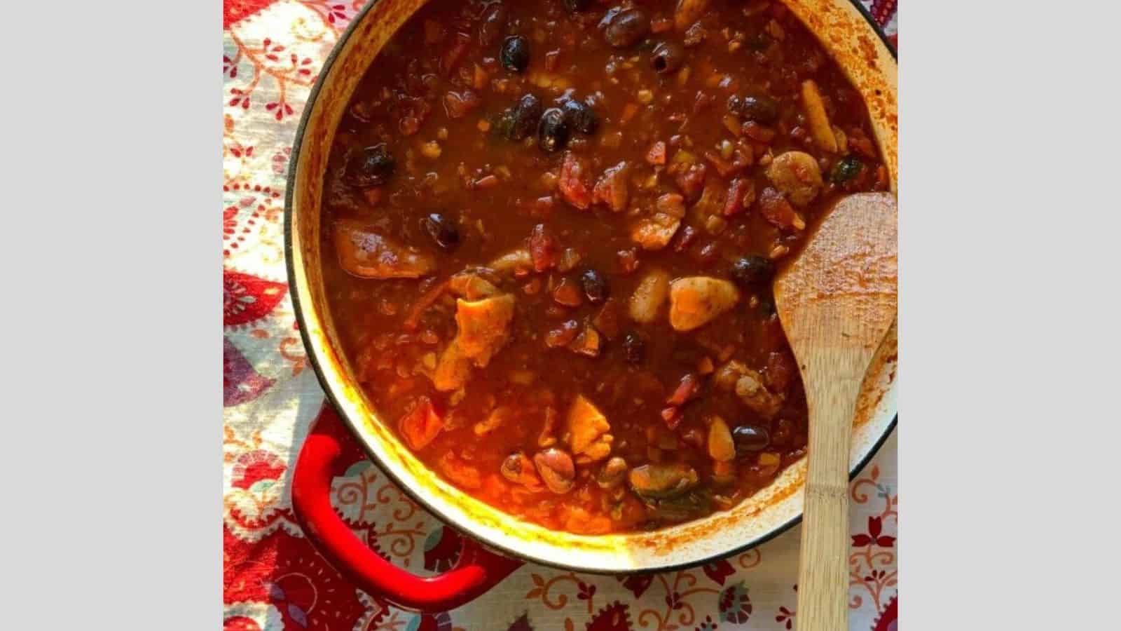 A Dutch oven filled with chicken cacciatore and a wooden spoon.