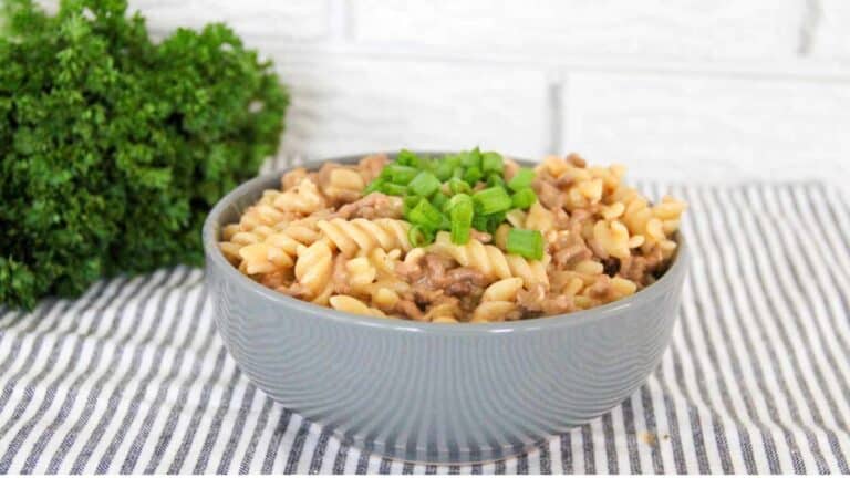 A bowl of pasta with meat and greens.