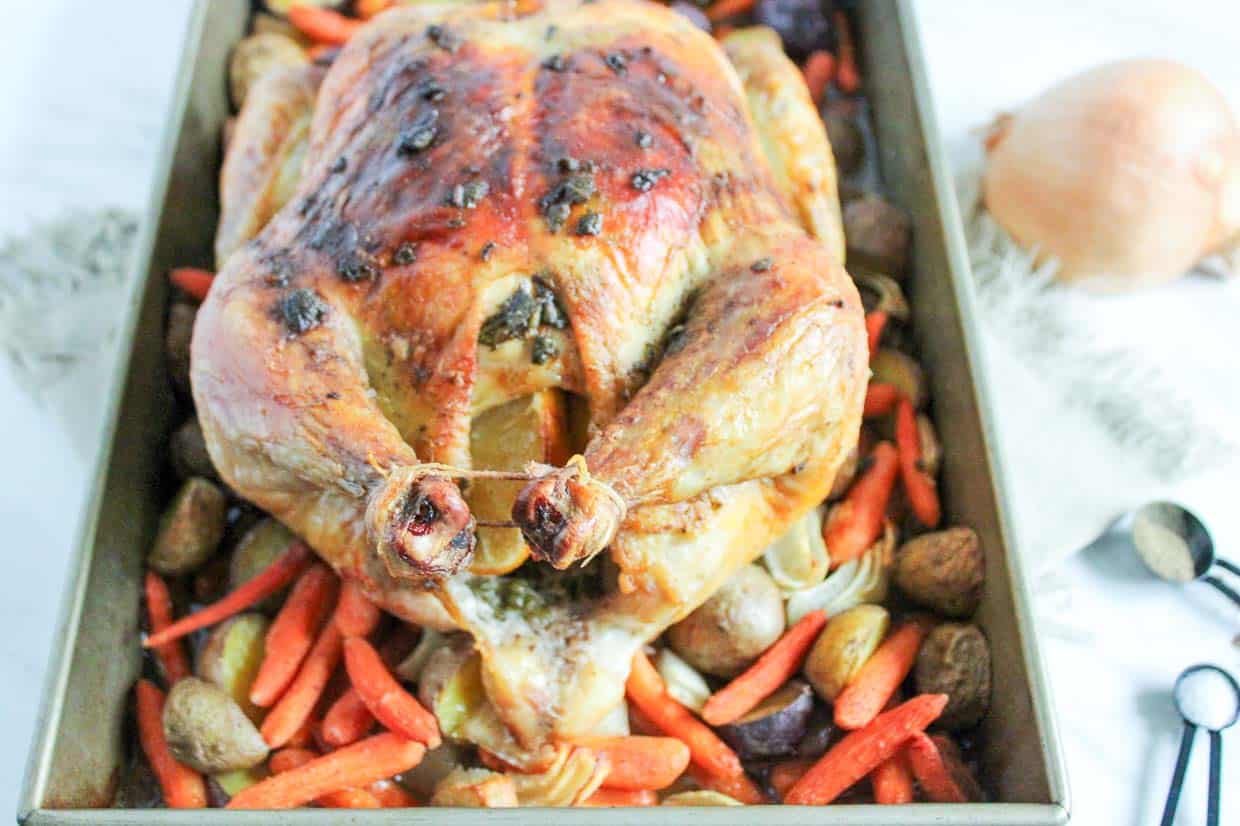 Roasted chicken nestled amongst potatoes, onions, and carrots in the baking pan.