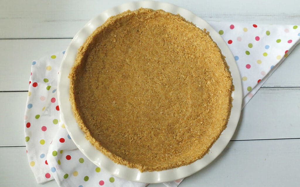 A freshly baked graham cracker pie crust on a white plate.