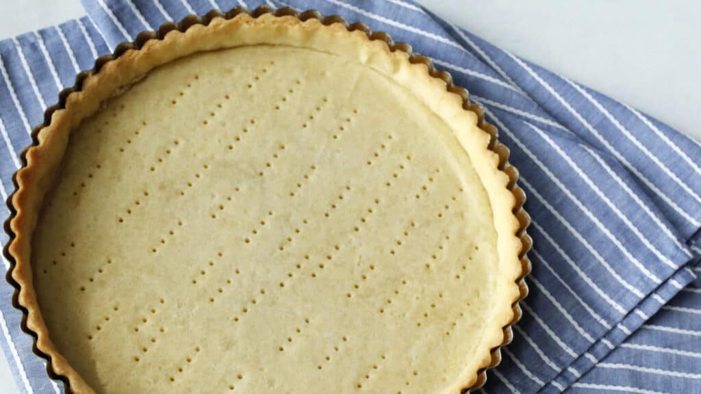 An unbaked pie crust with fork holes on a striped cloth.