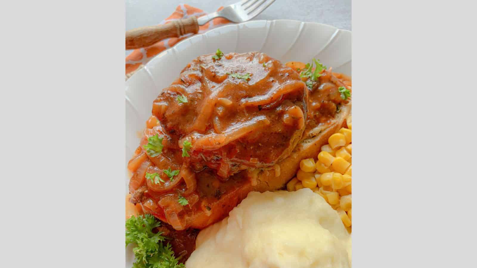 Salisbury Steak with brown gravy on cheese toast with corn and mashed potatoes on a dinner plate.