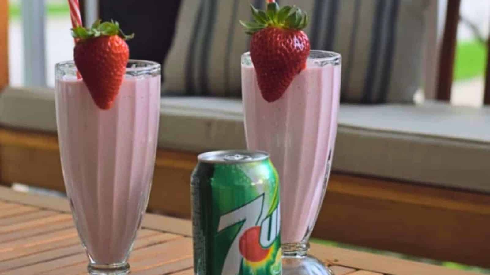 Two milkshake glasses with frozen strawberry lemonade garnished with strawberries sitting on a wooden table outside.