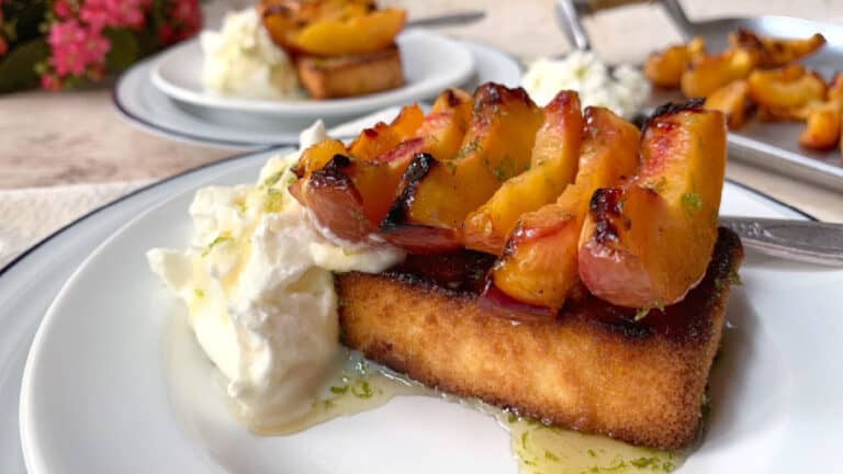 Grilled peaches on toasted bread with a side of creamy cheese, served on a plate.