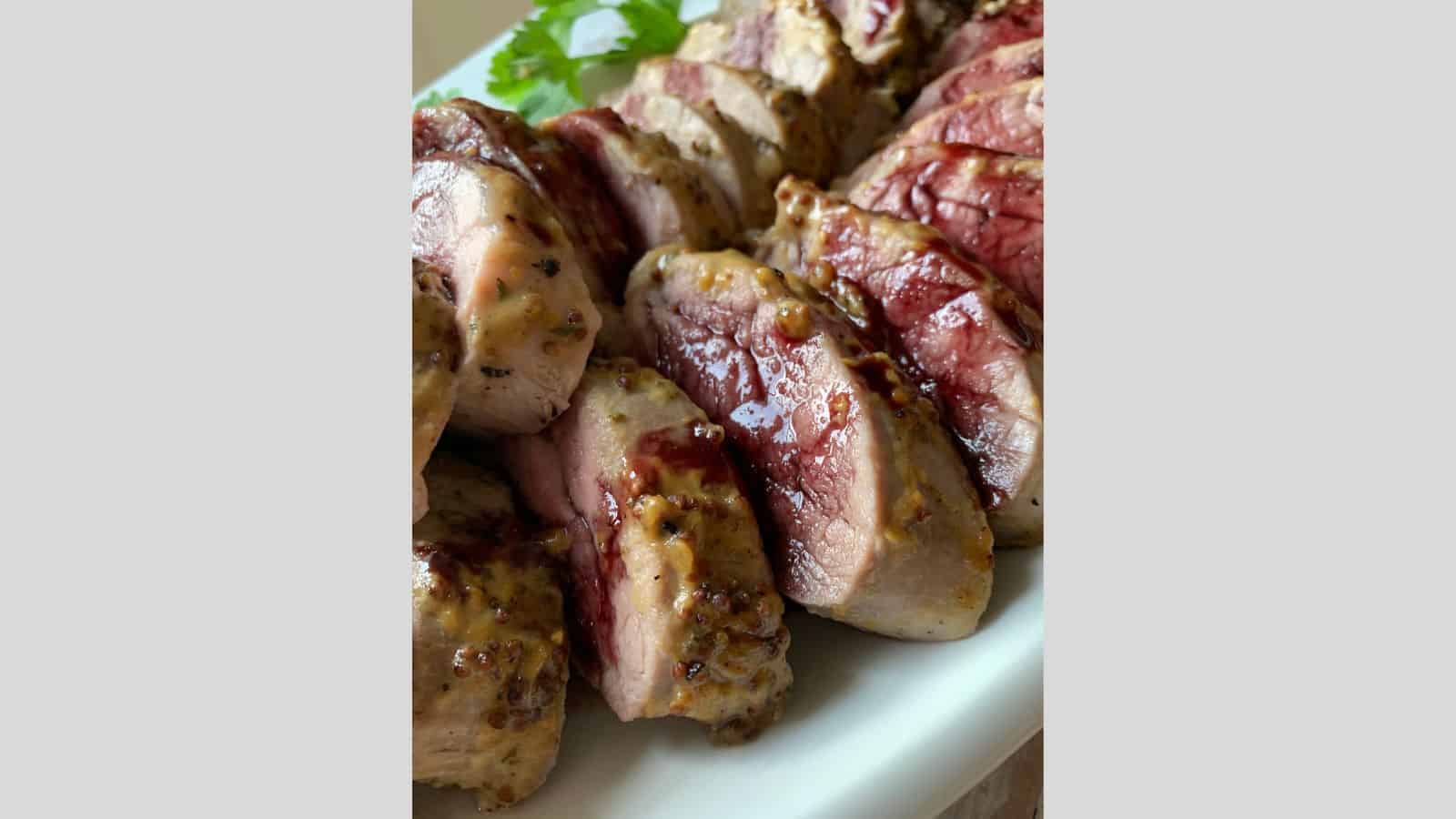 A platter with sliced pork tenderloin medallions drizzled with a red wine sauce.