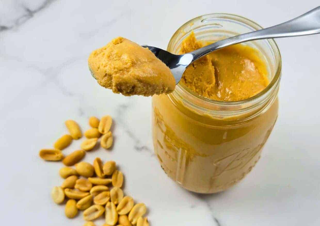 A mason jar of homemade peanut butter surrounded by a handful of peanuts.