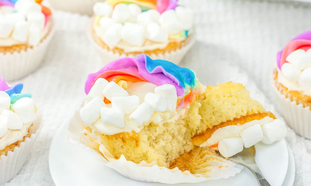 A rainbow cupcake with a piece cut off by a fork.