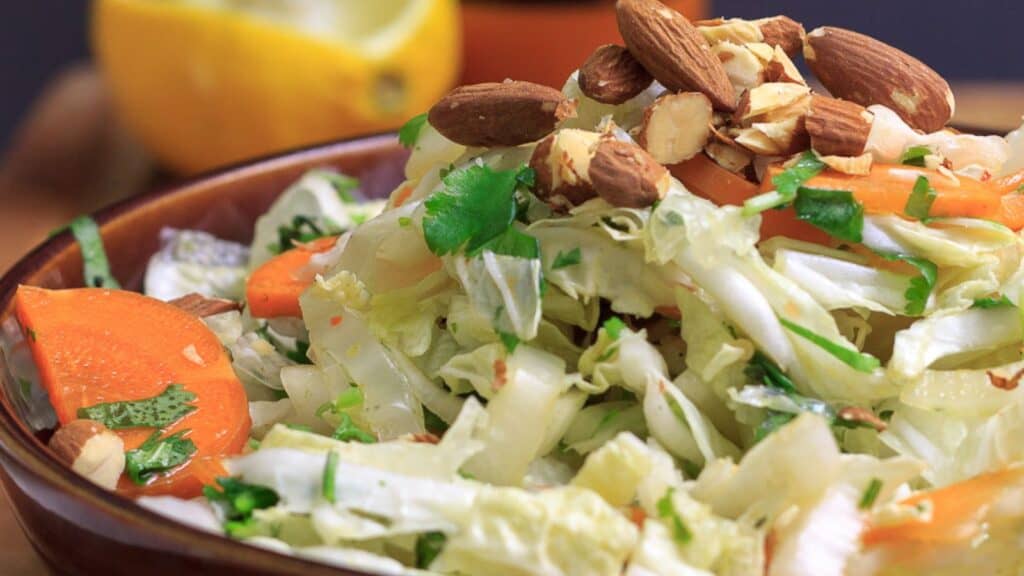 A bowl of cabbage salad with almonds and nuts.