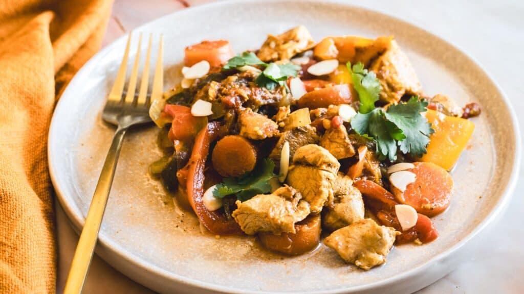 A colorful plate of stir-fry chicken and vegetables garnished with nuts and herbs.