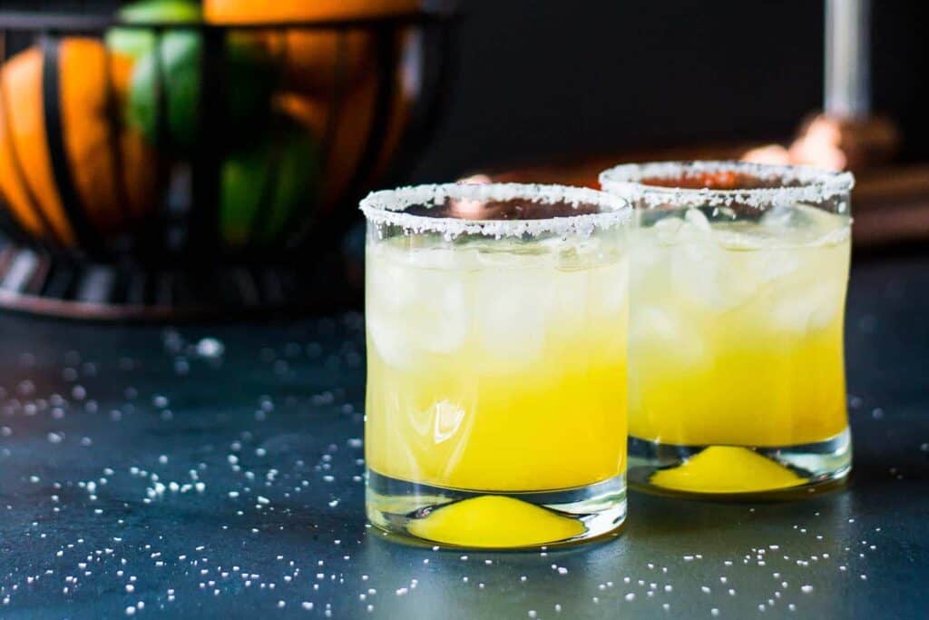 Two glasses of orange margarita on a table.