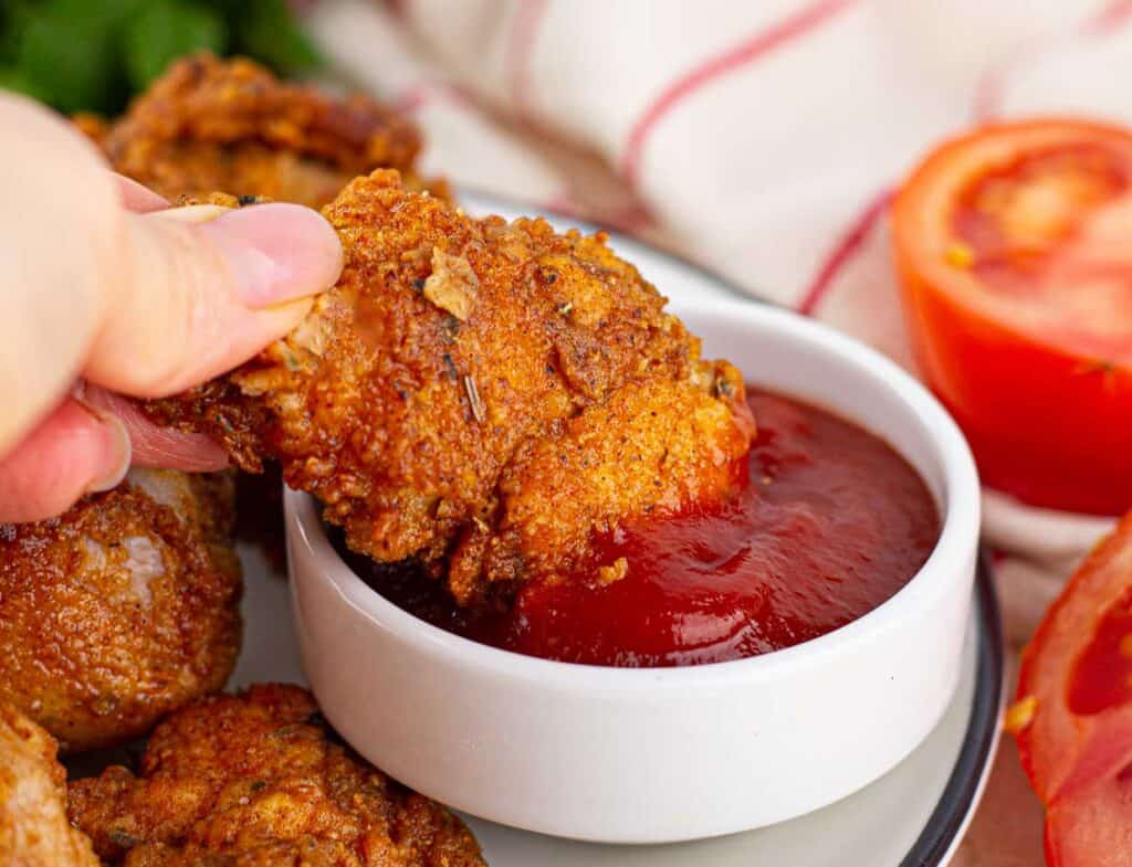 Crispy fried chicken served with ketchup and garnished with fresh tomato slices.